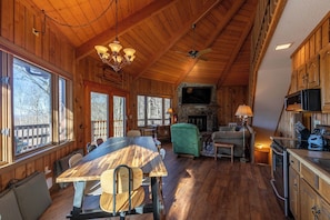 Ein Holzblockhaus-Interieur mit Esstisch, Stühlen, Kamin, Fernseher und Küchenzeile.