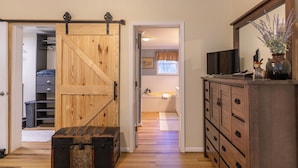 A room with a wooden sliding door, a dresser, a television, and a bathroom with a window. - Our Happy Nest (Boone)
