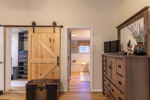A room with a wooden sliding door, a dresser, a television, and a bathroom with a window. - Our Happy Nest (Boone)