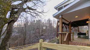 A wooden deck with a metal railing, overlooking a forested area. - Our Happy Nest (Boone)