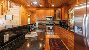 A modern kitchen with wooden cabinets, stainless steel appliances, a granite countertop, and a red patterned rug. - Morris Cabin (Boone)