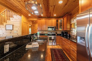 A modern kitchen with wooden cabinets, stainless steel appliances, a granite countertop, and a red patterned rug. - Morris Cabin (Boone)