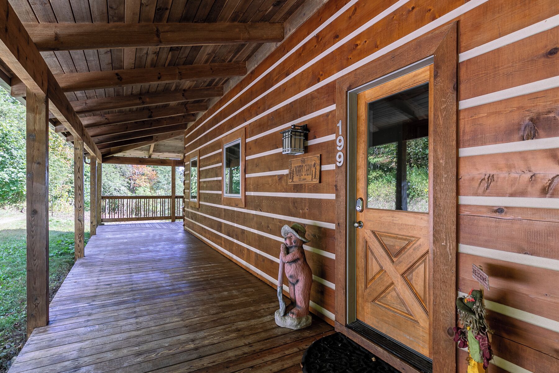 Une cabane en bois dotée d’un porche abrité, d’une pancarte de bienvenue et d’une statue d’ours.