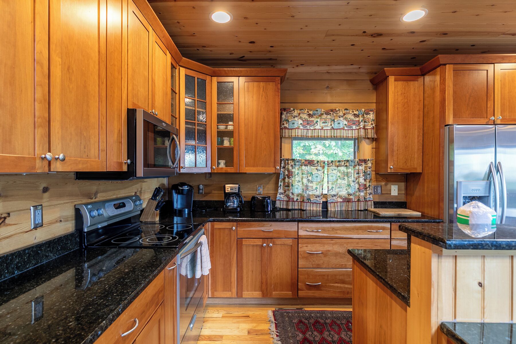 A kitchen with wooden cabinets, a stainless steel refrigerator, a microwave, and a stove.