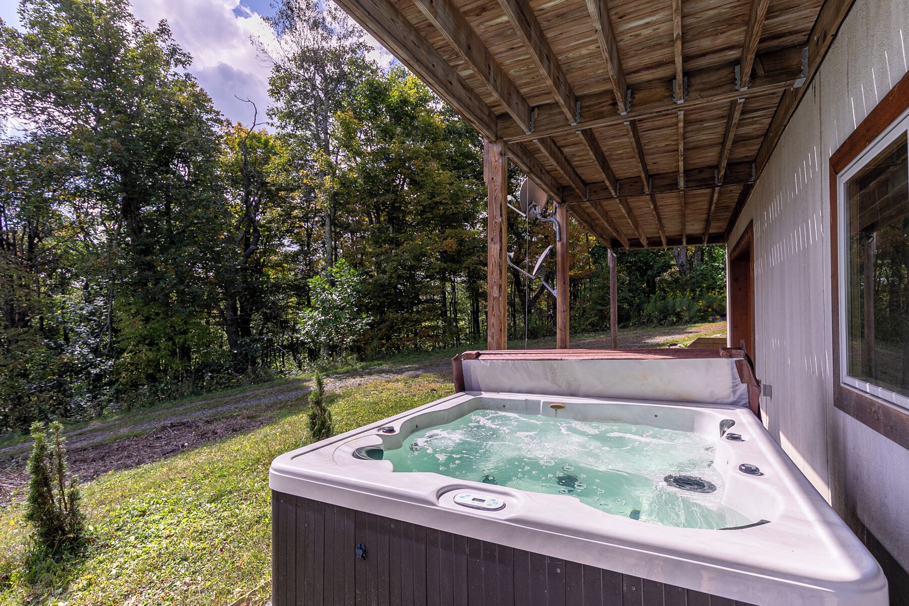 Un bain à remous sous une pergola en bois, avec vue sur une zone boisée.