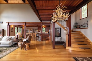A spacious living room with a wooden staircase, a dining area, and a kitchen. - Haven at Headwaters Long-range Mountain Views, Pet Friendly With Game Room (Elk Park)