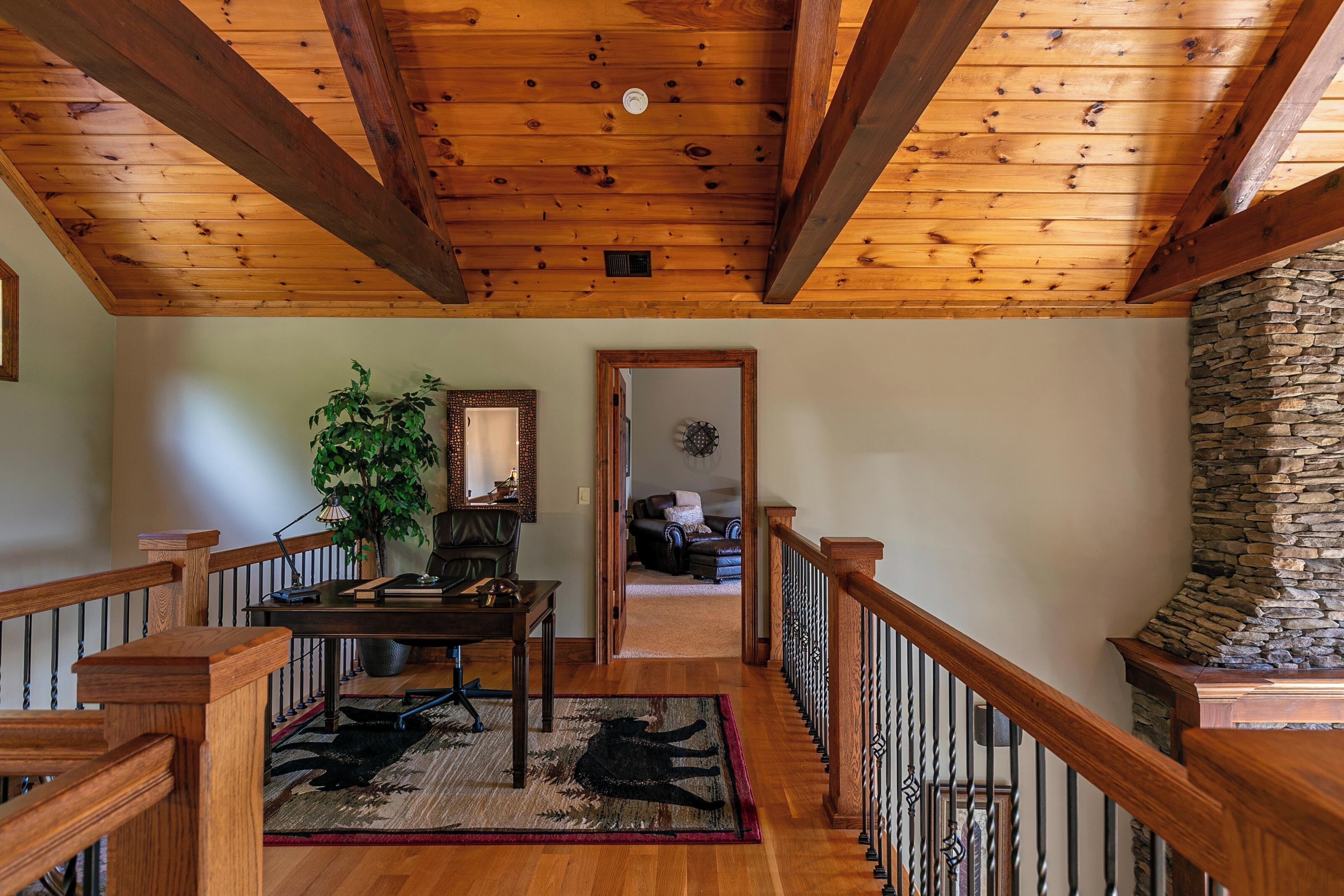 A wooden-floored hallway with a stone wall, a wooden railing, and a rug with a black silhouette.
