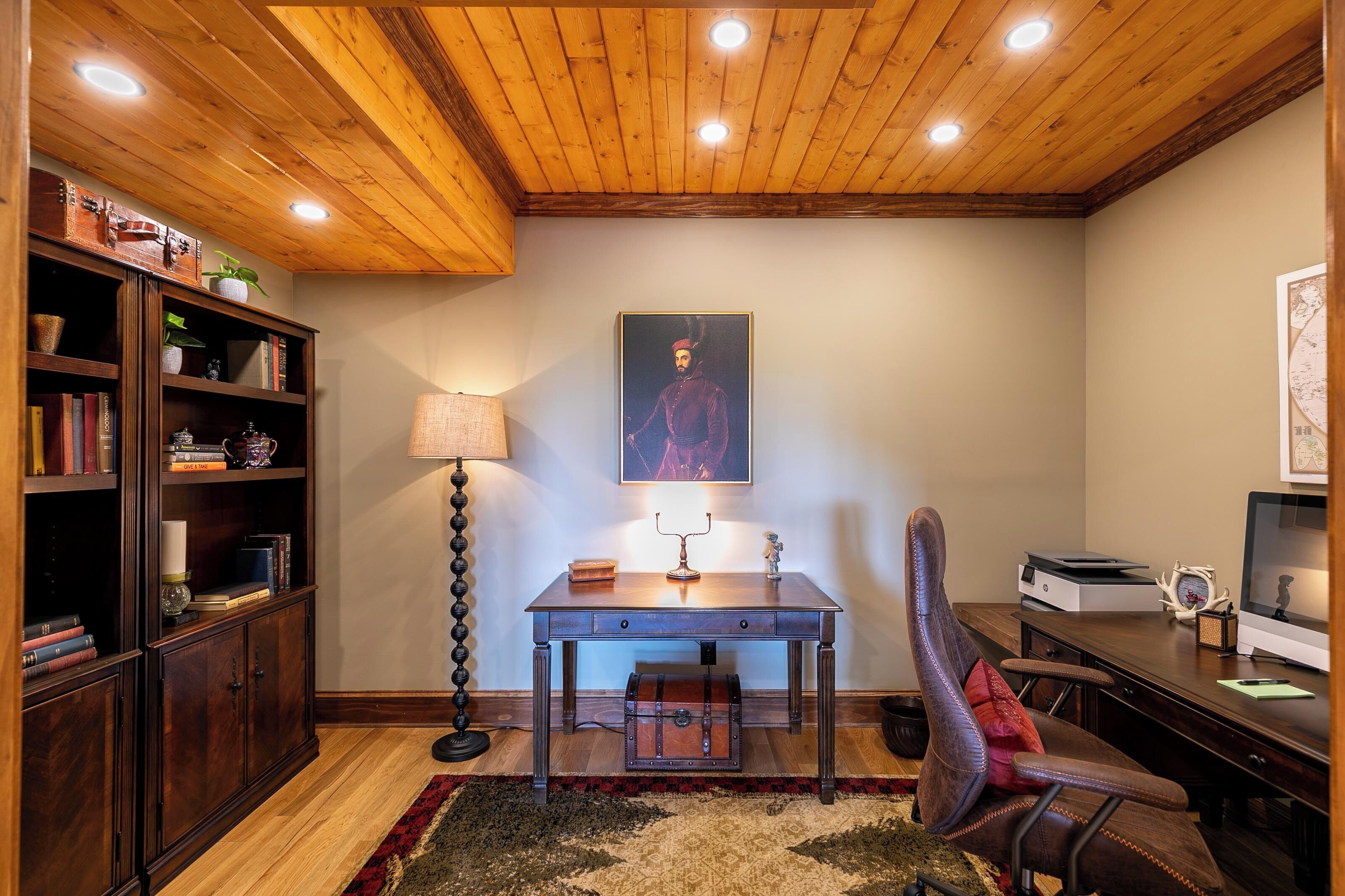 Una sala de estudio con un escritorio de madera, una estantería y un cuadro en la pared.