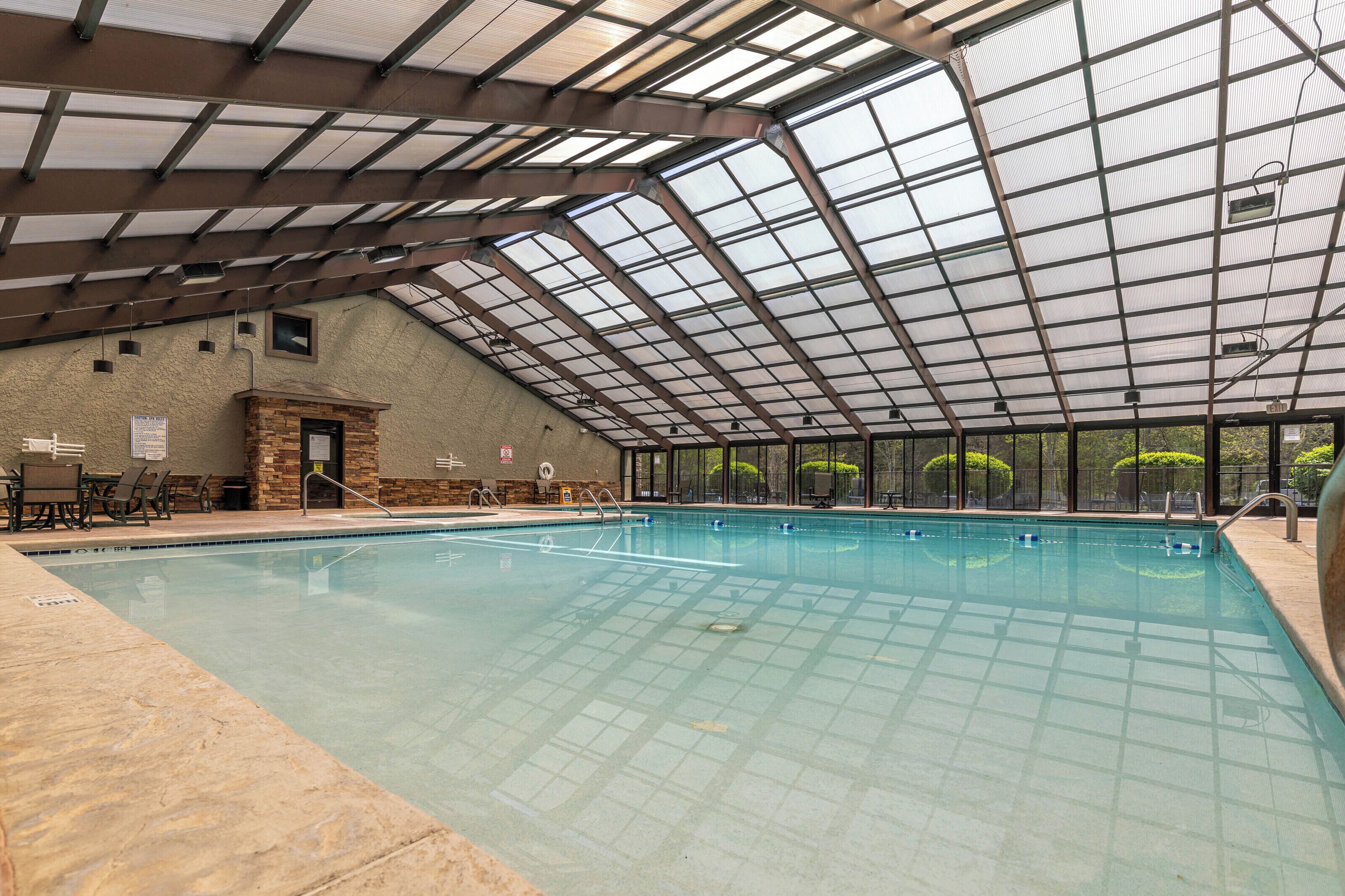 An indoor swimming pool with a glass ceiling, stone walls, and a small stone fireplace.