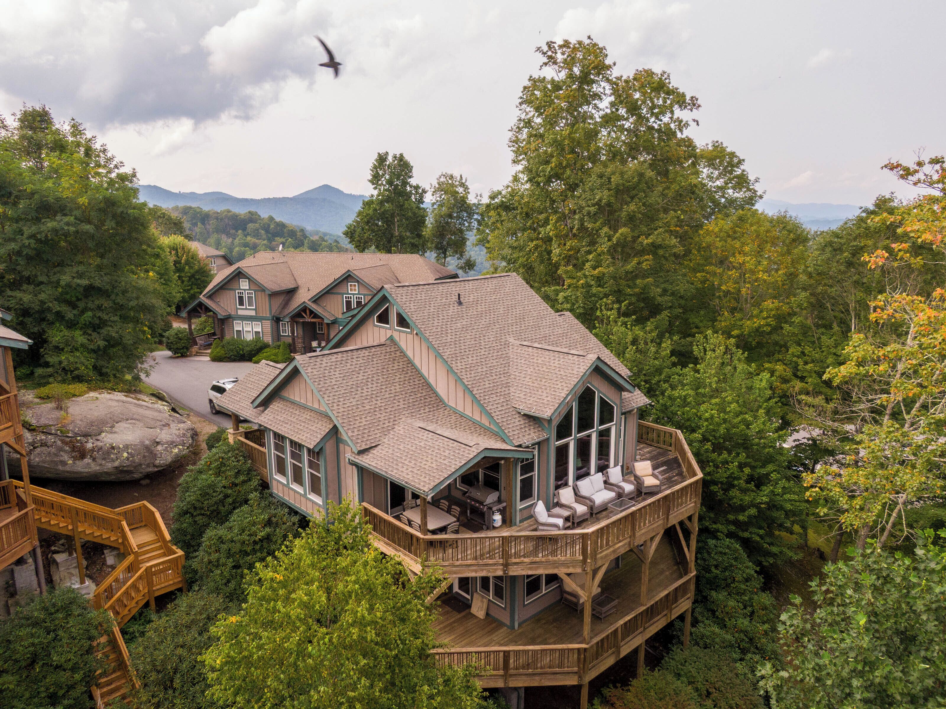 Ein mehrstöckiges Holzhaus mit Terrasse, umgeben von dichtem Wald und Bergen im Hintergrund.