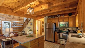 Interior de una cabaña de madera con cocina que incluye refrigerador, horno, microondas y armarios de madera.