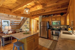 A wooden cabin interior with a kitchen featuring a refrigerator, oven, microwave, and wooden cabinets.