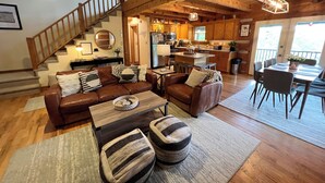 Amplia sala de estar con escalera de madera, cocina con armarios de madera y comedor con mesa y sillas.
