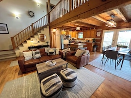 A spacious living area with a wooden staircase, a kitchen with wooden cabinets, and a dining area with a table and chairs.