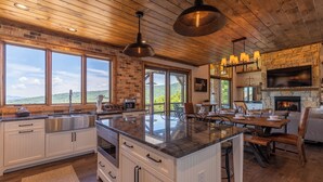 A spacious kitchen with a large island, wooden ceiling, and a stone fireplace. - Breezeway Lodge at Eagles Nest (Banner Elk)