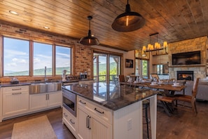A spacious kitchen with a large island, wooden ceiling, and a stone fireplace. - Breezeway Lodge at Eagles Nest (Banner Elk)