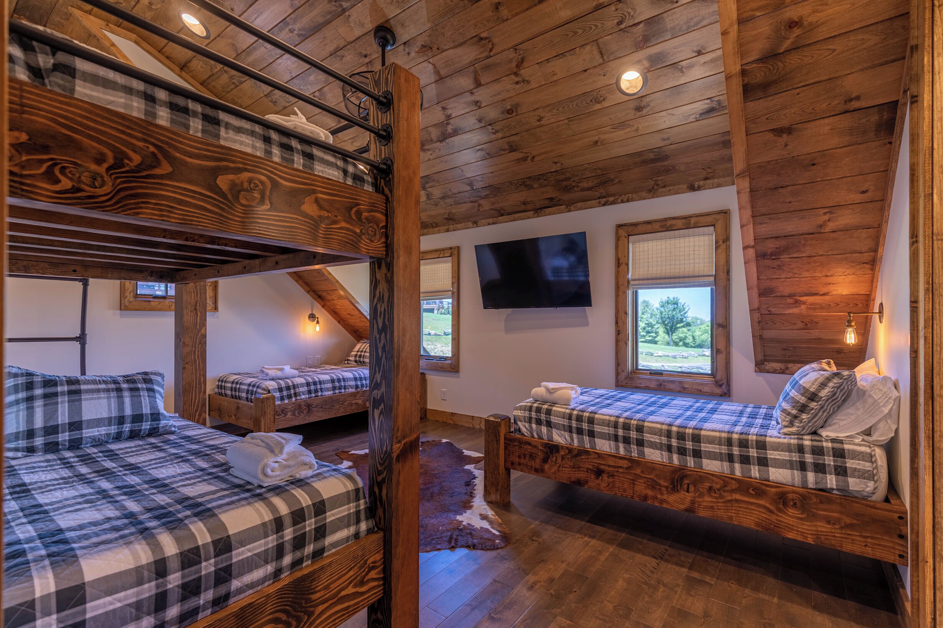 Une chambre de style rustique, aménagée comme un chalet, avec trois lits superposés, des poutres en bois, une télévision et une fenêtre donnant sur l’extérieur.