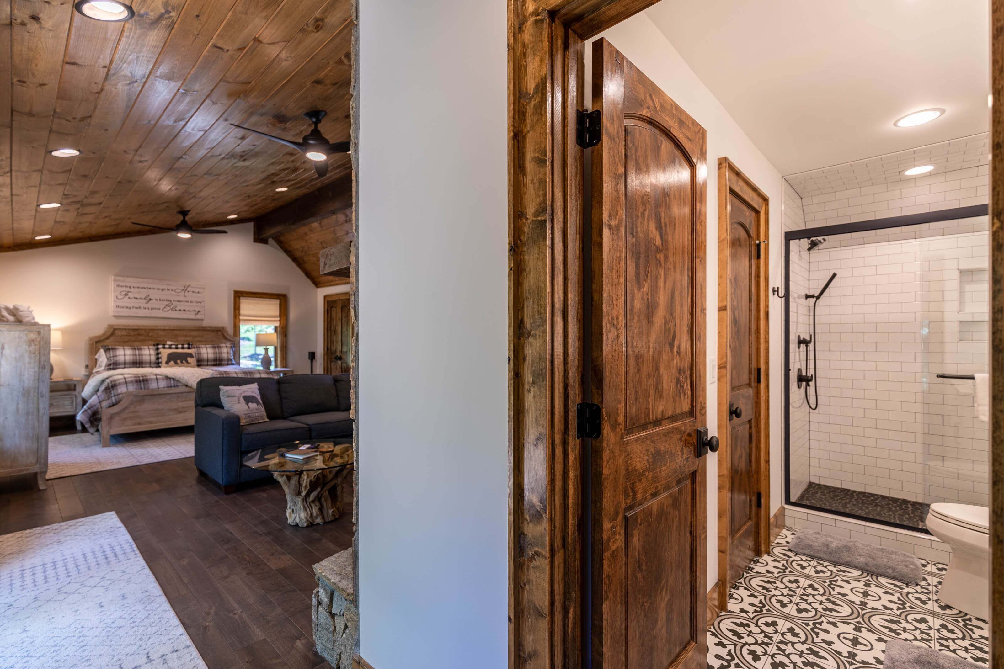 A room with a wooden ceiling, a bed with a plaid comforter, a dark sofa, and a small wooden coffee table.
