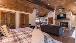 A spacious living area with a large bed, a sofa, a fireplace, and a television mounted on a stone wall. - Breezeway Lodge at Eagles Nest (Banner Elk)