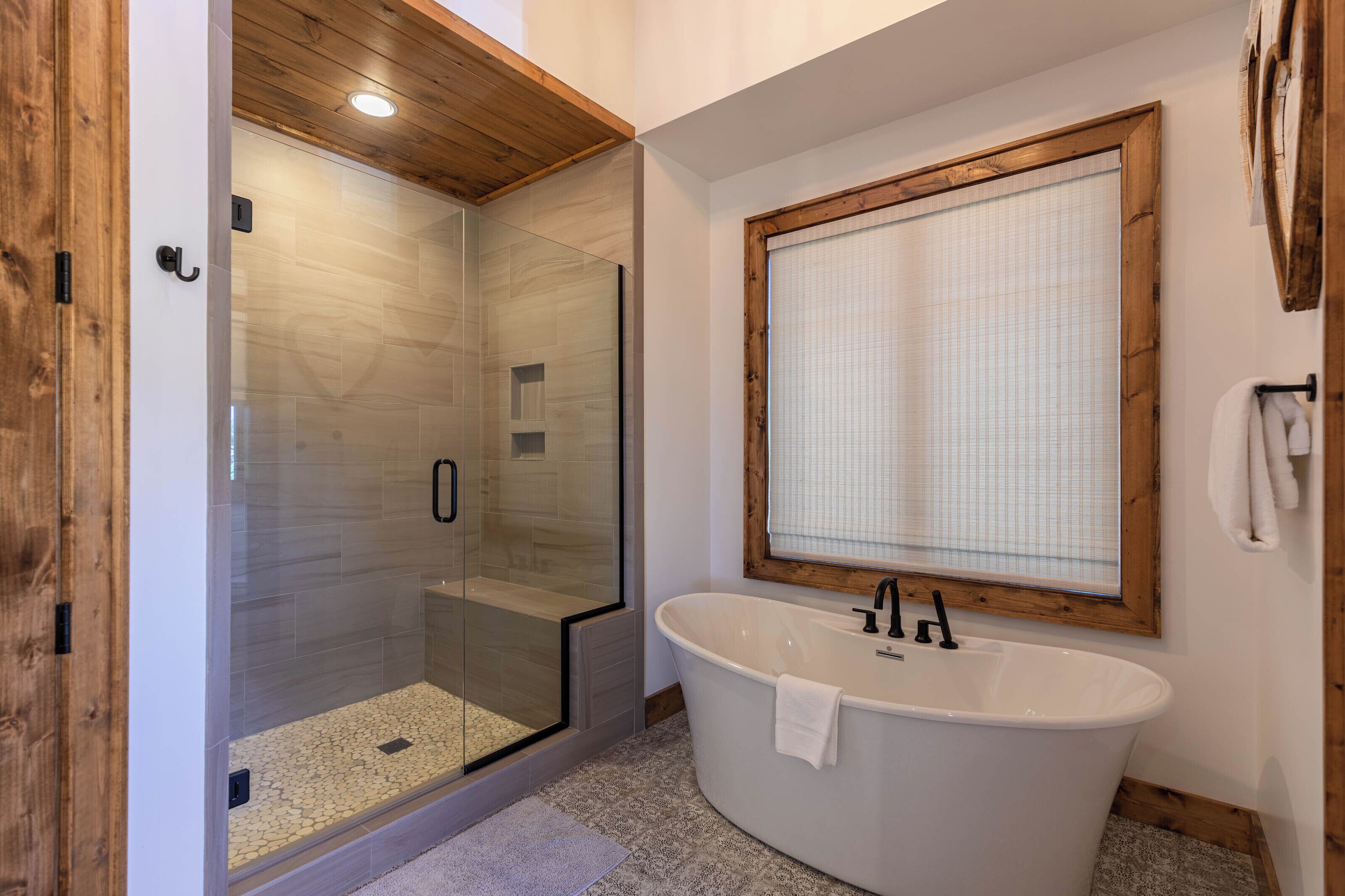 A modern bathroom with a glass-enclosed shower, a freestanding bathtub, and a large mirror with a wooden frame.
