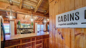 Een rustiek interieur van een blokhut, met een stenen open haard, houten kastjes en een bordje met de tekst 'CABINS. Vraag binnen'.