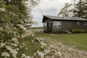 A single-story house with a large window, a door, and a small porch. - Renovated Vintage 1970s Lake Cottage in Iola—30 Min to Chain O'Lakes (Iola)