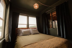 A bedroom with a bed, two windows, and a hanging light fixture. - Renovated Vintage 1970s Lake Cottage in Iola—30 Min to Chain O'Lakes (Iola)