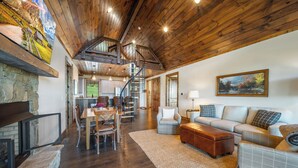 A spacious living area with a wooden ceiling, a fireplace, a dining area, and a staircase leading to an upper level. - Campfire Trail at Eagles Nest - pet Friendly (Banner Elk)