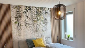 Une chambre moderne avec un lit, une lampe fixée au mur et une fenêtre agrémentée d’une plante.