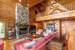 A log cabin interior with a stone fireplace, a balcony, and a cozy seating area. - Four Points With Mountain Views, King With Fireplace on Main, hot Tub, pet Friendly (Vilas)