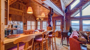 A log cabin interior with a wooden bar, seating area, and large windows.
