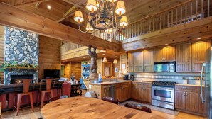 A spacious kitchen with wooden cabinets, a large island, and a stone fireplace.