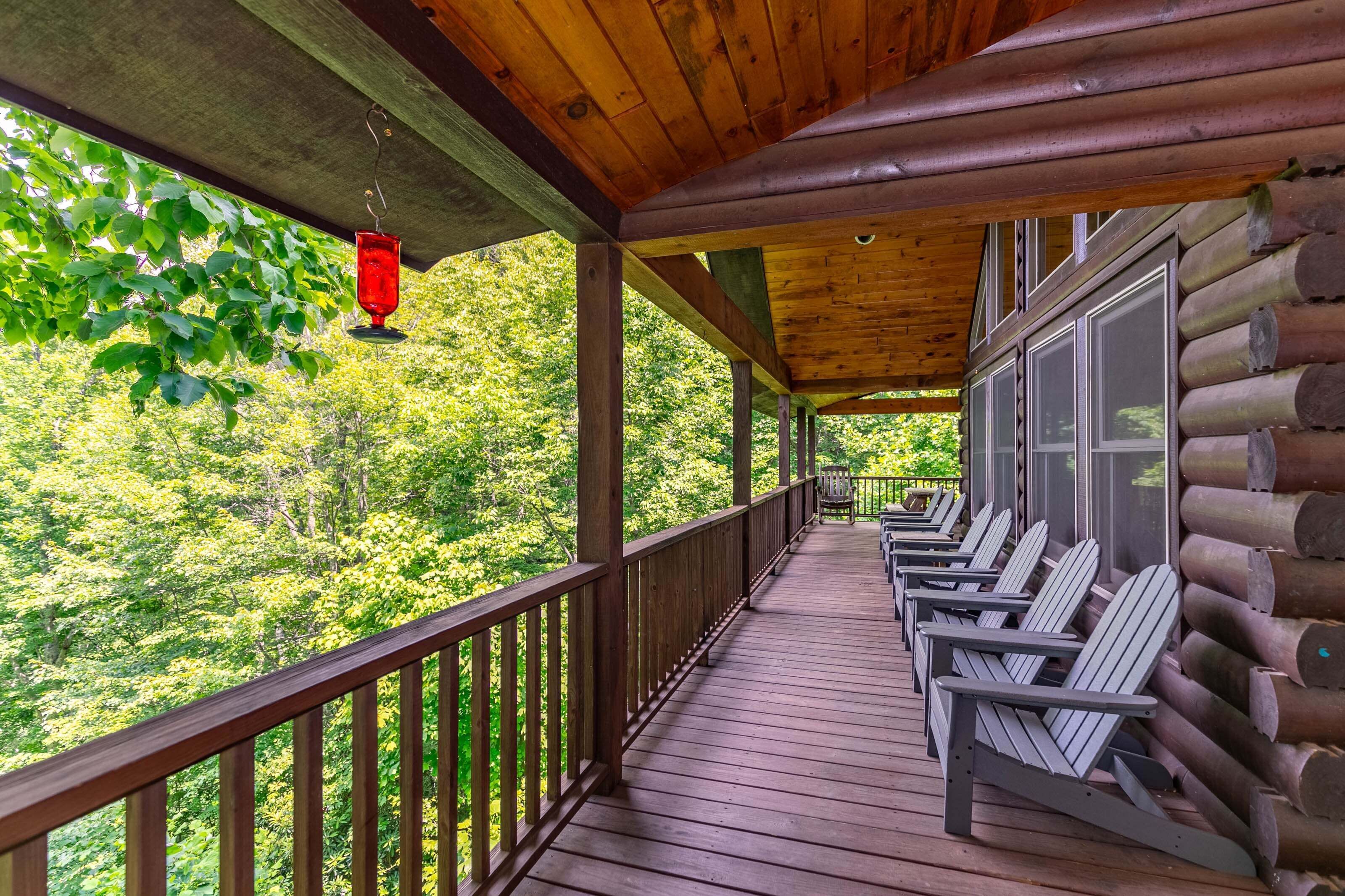 A wooden deck with Adirondack chairs, a hanging red lantern, and a view of a forested area.