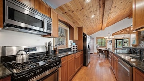 Una cocina con estufa de acero inoxidable, microondas y refrigerador, armarios de madera y techo de madera.
