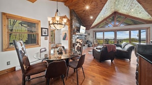 Amplia sala de estar con una mesa de comedor de vidrio, piso de madera y chimenea de piedra.
