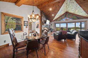 Amplia sala de estar con una mesa de comedor de vidrio, piso de madera y chimenea de piedra.