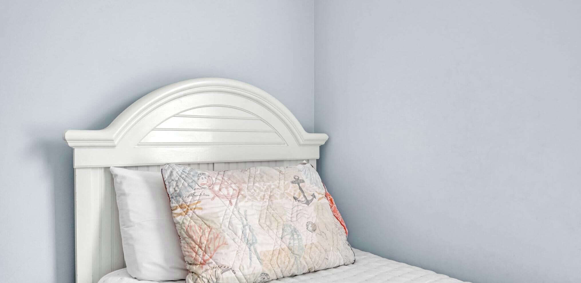 A bed with a white headboard and a decorative pillow with a nautical theme.