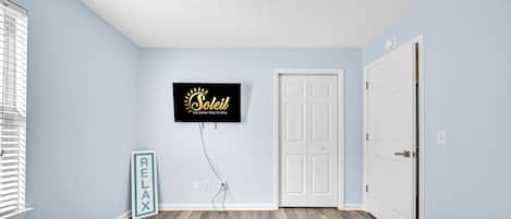 Un dormitorio con dos camas, un televisor montado, un cartel de relajación y una puerta.
