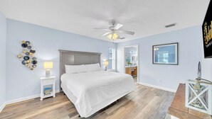 A bedroom with a bed, a ceiling fan, a wall art piece, and a nightstand with books. - Cottage on Cabana Private Gated Neighborhood (Panama City Beach)