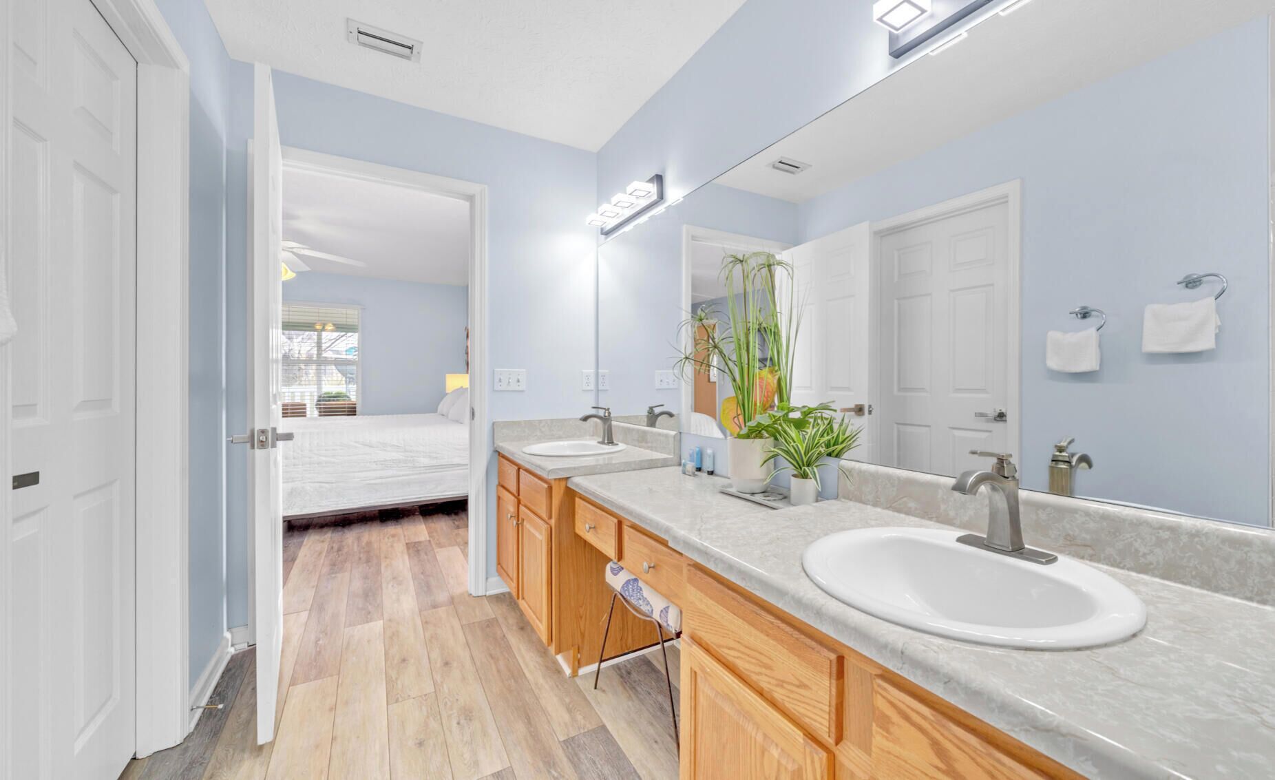 A modern bathroom with two sinks, wooden cabinets, a large mirror, and a potted plant.