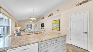 A kitchen with granite countertops, white cabinets, a dining area with chairs, and a large white door. - Cottage on Cabana Private Gated Neighborhood (Panama City Beach)