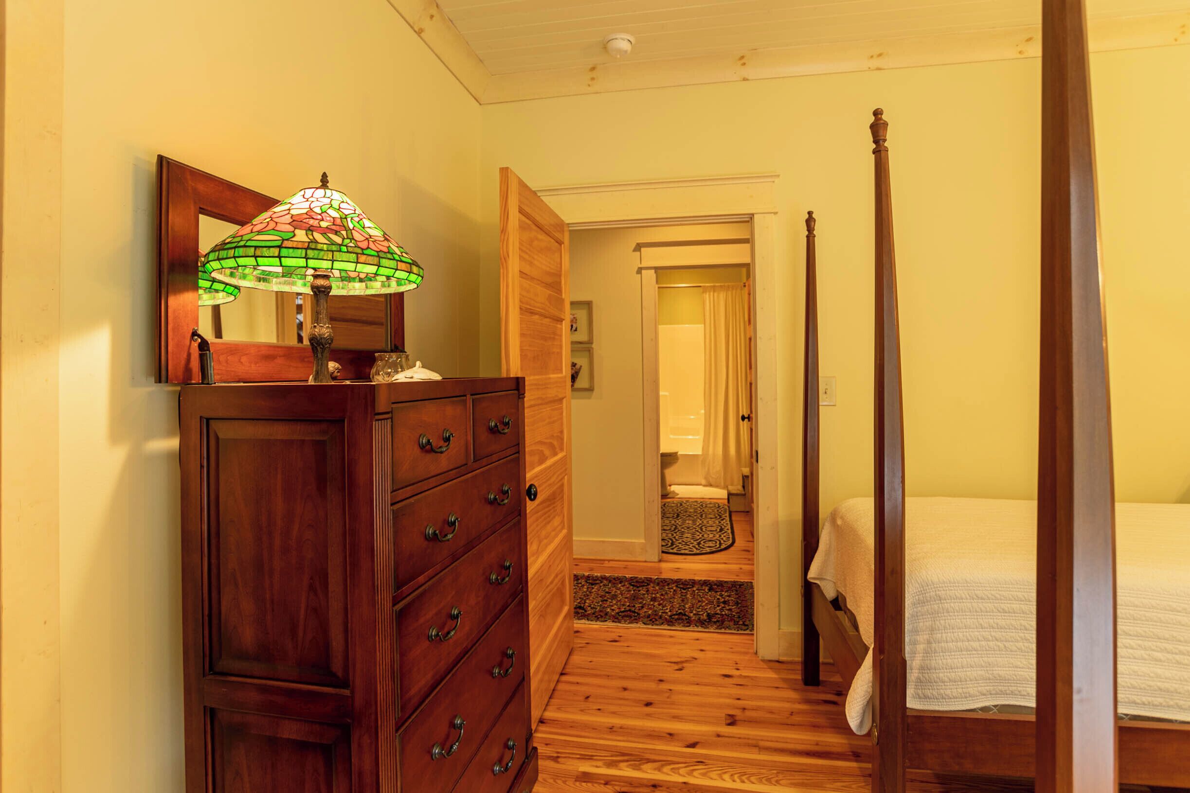 A bedroom with a four-poster bed, wooden dresser, and a stained glass lamp.