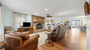 A living room with a stone fireplace, leather sofas, wooden flooring, and a television.