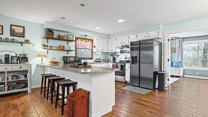 A modern kitchen with white cabinetry, a large island with stools, a stainless steel refrigerator, and a window with a view.