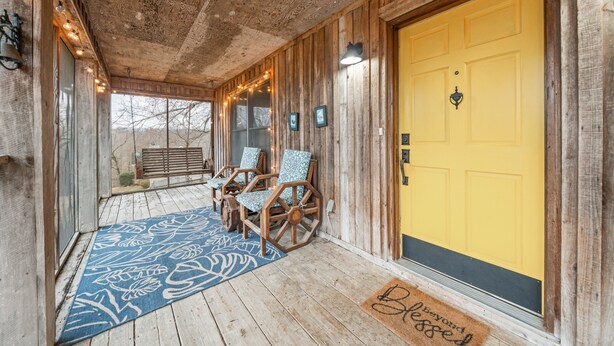 A wooden porch with a yellow door, rocking chairs, and a blue patterned rug.