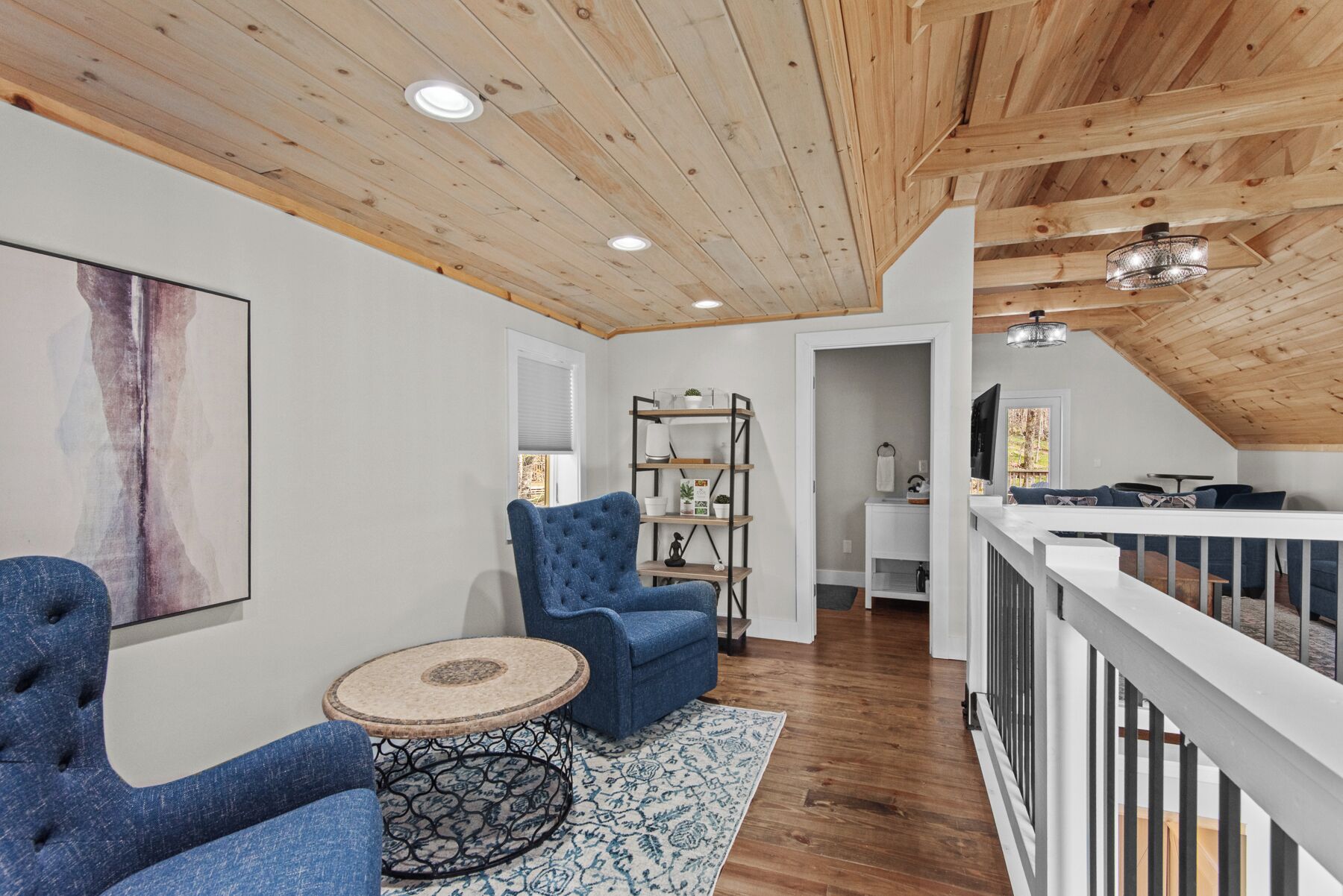 A loft-style room with a wooden ceiling, a blue armchair, a round table, and a bookshelf.