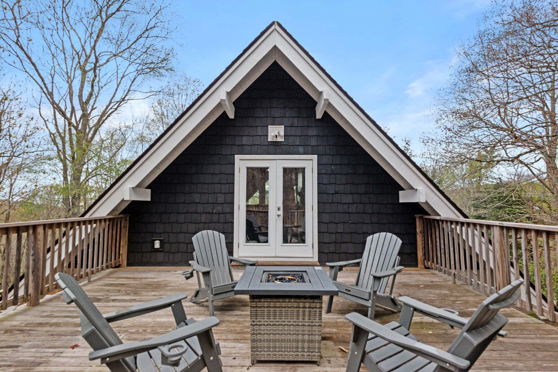 Eine schwarze Holzhütte mit weißer Tür und Fenstern, eine Terrasse mit Stühlen und Tisch sowie ein Holzzaun, der die Terrasse umgibt.