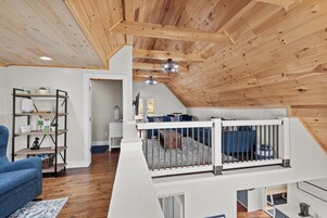 A loft-style room with a wooden ceiling, a white railing, a sofa, and a bookshelf.