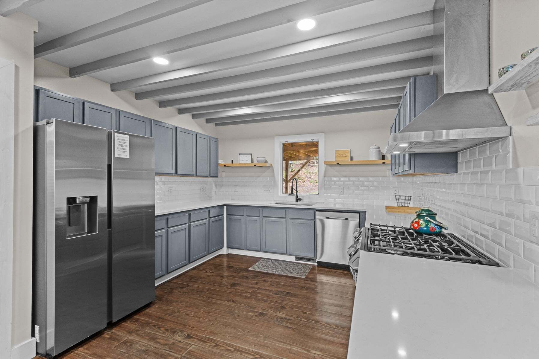 A modern kitchen with grey cabinets, a stainless steel refrigerator, a gas stove, and a window with a view.