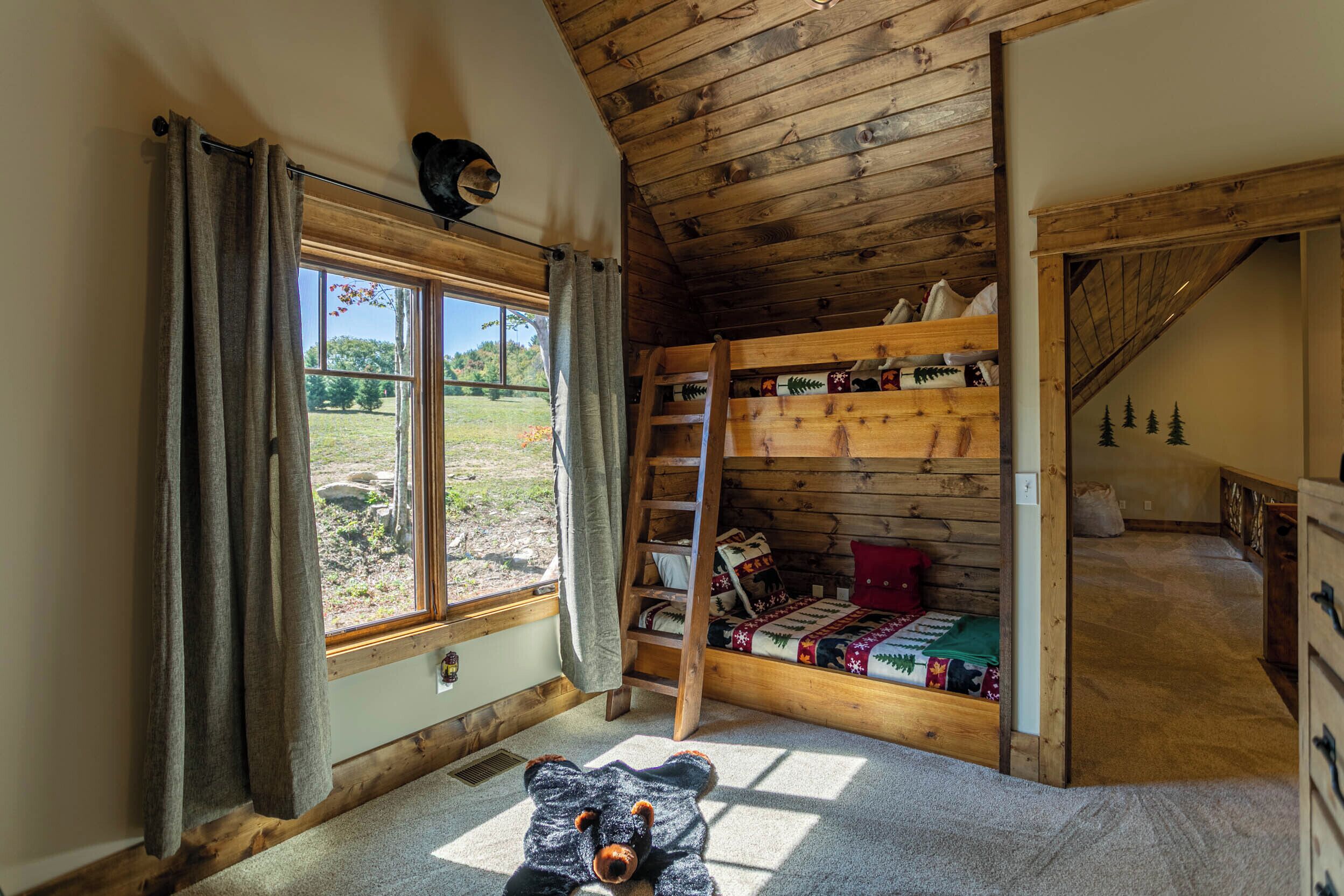 A cozy cabin room with a bunk bed, a ladder, a window with curtains, and a teddy bear on the floor.